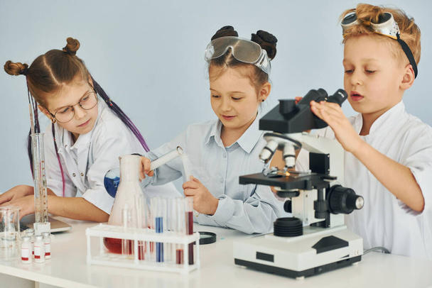 Using microscope. Children in white coats plays a scientists in lab by using equipment. - Photo, image