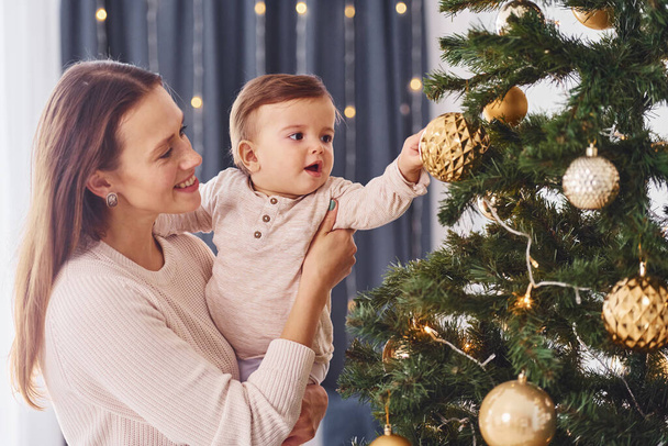 Decorating Christmas tree. Mother with her little daughter is indoors at home together. - Fotografie, Obrázek