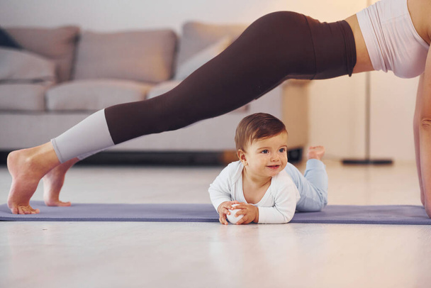 Woman doing exercises. Mother with her little daughter is at home together. - Foto, Bild