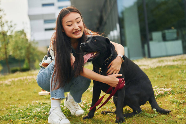 Playing with dog. Young asian woman is outdoors at daytime. - Zdjęcie, obraz