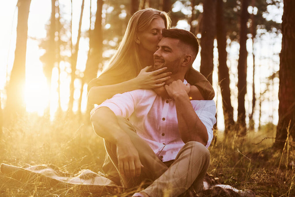 Sitting on the ground. Happy couple is outdoors in the forest at daytime. - Foto, Imagen