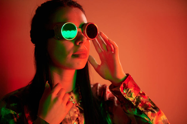 In retro pilot glasses. Fashionable young woman standing in the studio with neon light. - Foto, Imagen