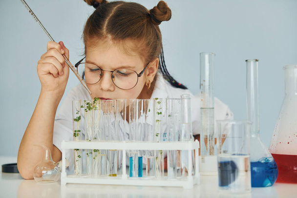 Workes with liquid that is in test tubes. Little girl in coat playing a scientist in lab by using equipment. - Foto, imagen