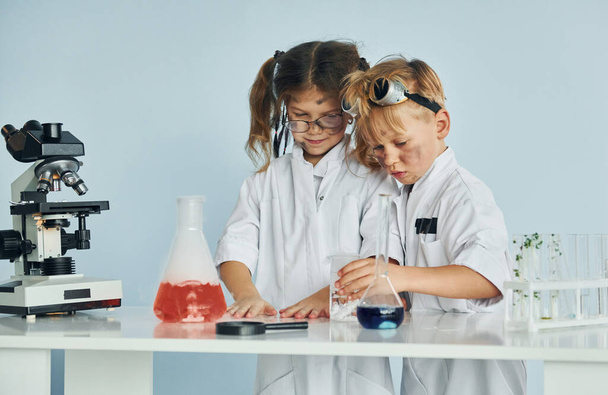 Little girl and boy in white coats plays a scientists in lab by using equipment. - 写真・画像