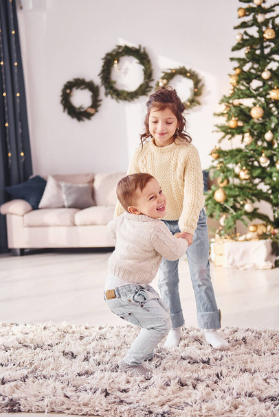 Active time spending. Little brother and sister is at christmas decorated room together. - Fotografie, Obrázek