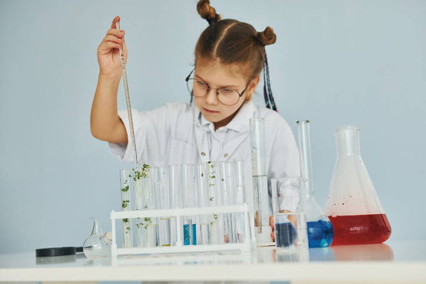 Workes with liquid that is in test tubes. Little girl in coat playing a scientist in lab by using equipment. - Photo, image