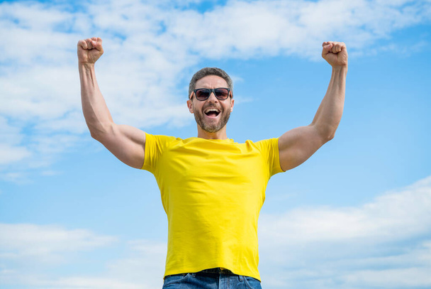 happy muscular man in yellow shirt and sunglasses on sky background. - Photo, image