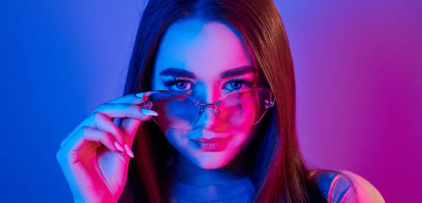 Neutral facial expression. Fashionable young woman standing in the studio with neon light. - 写真・画像