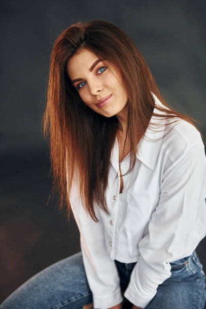In white shirt and blue jeans. Young beautiful woman is posing for the camera in the studio. - Fotoğraf, Görsel