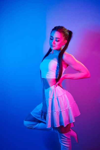 In skirt. Fashionable young woman standing in the studio with neon light. - Fotoğraf, Görsel