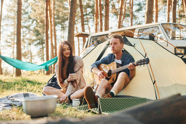 Sitting near the tent. Young couple is traveling in the forest at daytime together. - Foto, Imagen