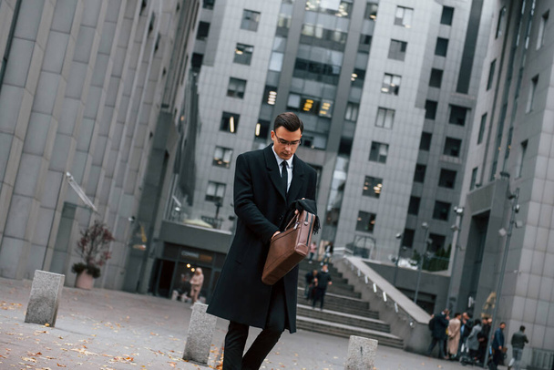 In formal clothes. Businessman in black suit and tie is outdoors in the city. - Foto, Imagen