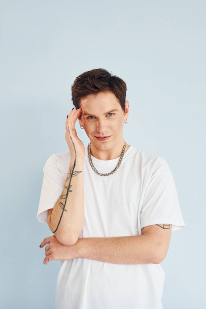 Young gay man is standing in the studio and posing for a camera. In casual white shirt. - Photo, image