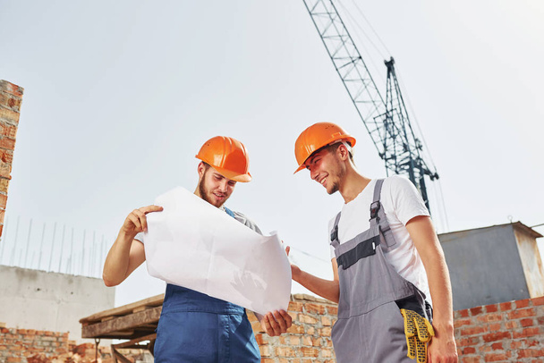 Reading plan. Two young construction workers in uniforms is busy at the unfinished building. - Foto, Bild