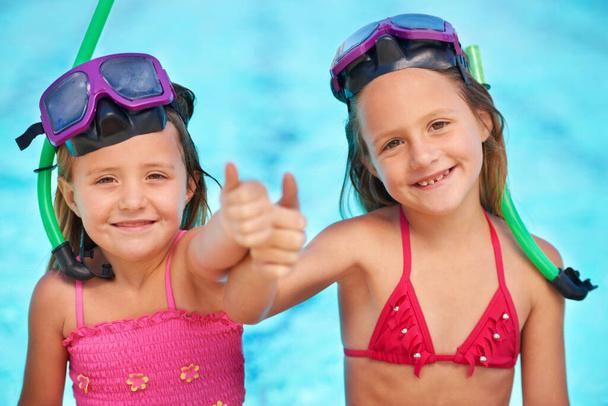 Rocas de verano. Dos niñas lindas mostrando los pulgares hacia arriba mientras en sus trajes de baño en la piscina - Foto, imagen