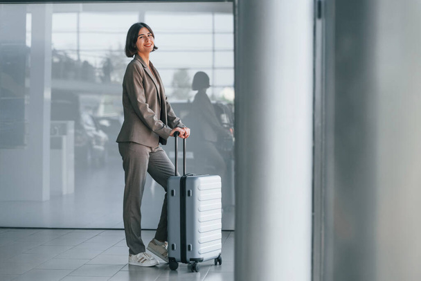 In formal clothes. Woman with luggage is standing indoors. Conception of tourism. - Photo, image
