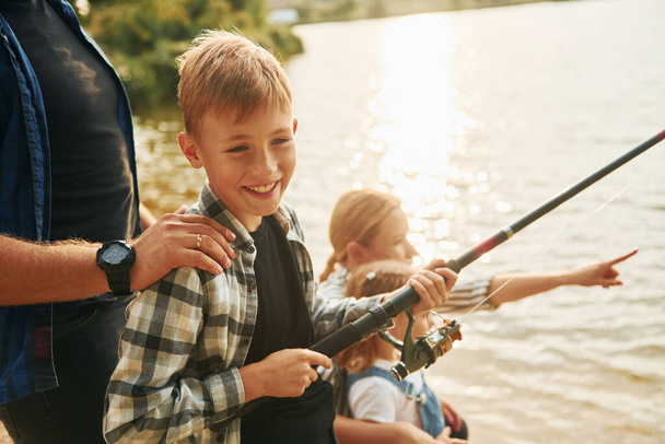 Learning to fishing. Father and mother with son and daughter together outdoors at summertime. - Zdjęcie, obraz