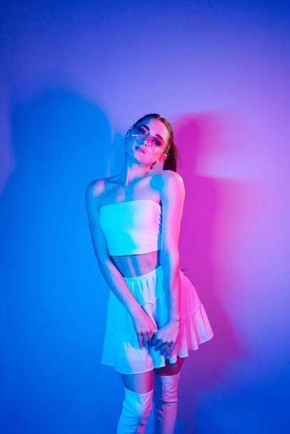 White clothes. Fashionable young woman standing in the studio with neon light. - Φωτογραφία, εικόνα