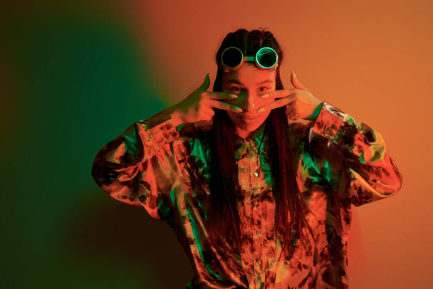 Retro eyewear. Fashionable young woman standing in the studio with neon light. - Fotó, kép
