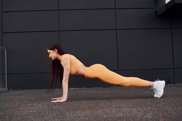 Doing push ups. Young woman in sportswear have fitness session outdoors. - 写真・画像