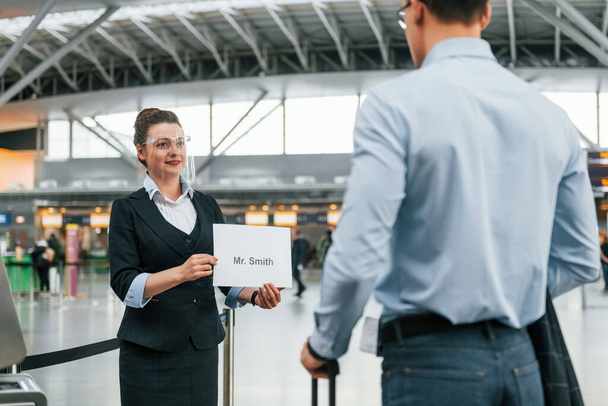 Meet by the woman with text. Young businessman in formal clothes is in the airport at daytime. - Fotoğraf, Görsel
