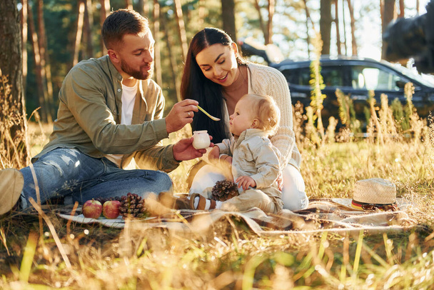 Eating some food. Happy family of father, mother and little daughter is in the forest. - Foto, Imagen