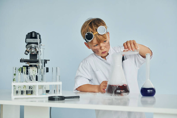 Little boy in coat playing a scientist in lab by using equipment. - Фото, зображення
