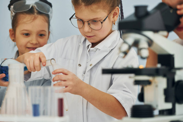 Mikroskoopilla. Valkotakkiset lapset esittävät tutkijaa laboratoriossa laitteiden avulla. - Valokuva, kuva