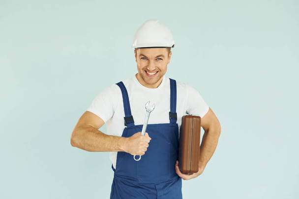 Holding brown case. Worker in uniform and hard hat standing in the studio with equipment. - Фото, изображение