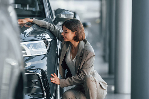 Embracing the car. Woman is indoors near brand new automobile indoors. - Foto, Imagem