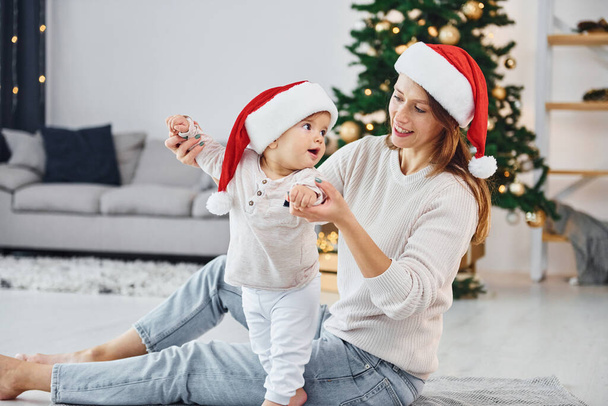 Celebrating Christmas. Mother with her little daughter is indoors at home together. - Foto, Imagem