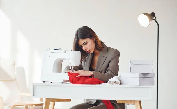 Seamstress working in the office. Young woman in formal clothes is indoors. Conception of style. - 写真・画像
