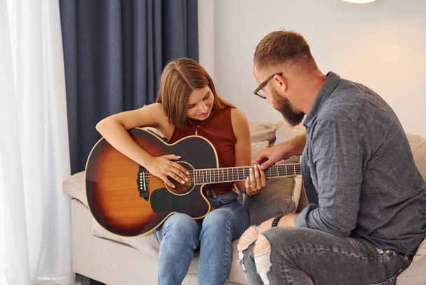 Private lesson. Guitar teacher showing how to play the instrument to young woman. - Foto, immagini