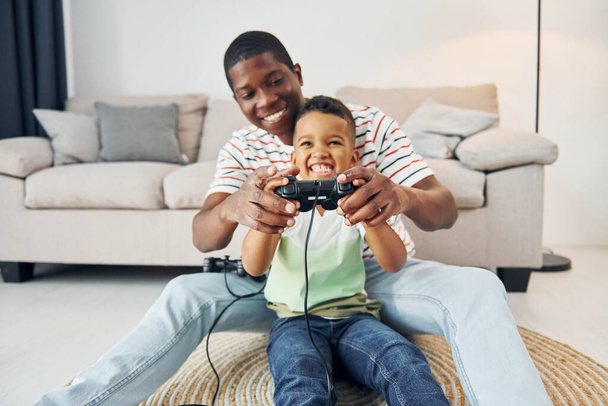 Using joysticks to play video game. African american father with his young son at home. - Foto, afbeelding