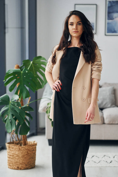 In black dress and jacket. European woman in fashionable stylish clothes is posing indoors. - Foto, Imagen