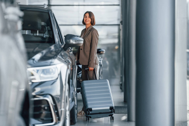 Holding luggage. Woman is indoors near brand new automobile indoors. - Fotografie, Obrázek