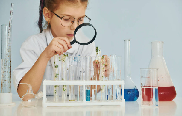 Workes with liquid that is in test tubes. Little girl in coat playing a scientist in lab by using equipment. - Foto, Bild