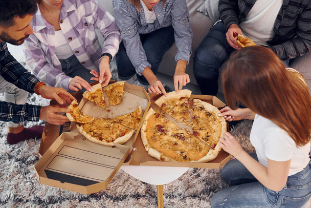 Ем вкусную пиццу. Группа друзей устраивает вечеринку в помещении вместе. - Фото, изображение