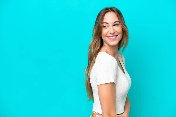 Young caucasian woman isolated on blue background looking to the side and smiling - Photo, Image