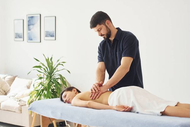 Mujer joven está acostado cuando el hombre haciendo masaje de su cuerpo en el spa. - Foto, Imagen