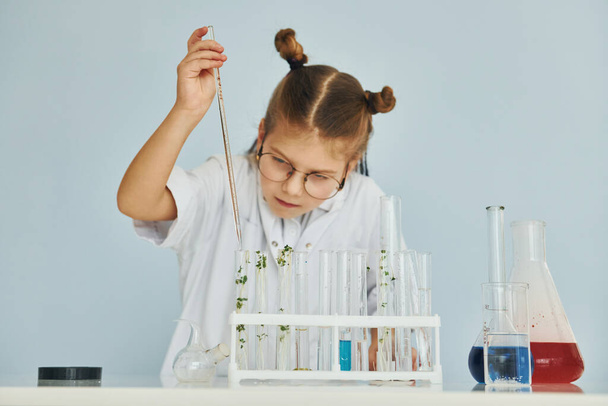 Workes with liquid that is in test tubes. Little girl in coat playing a scientist in lab by using equipment. - Foto, imagen