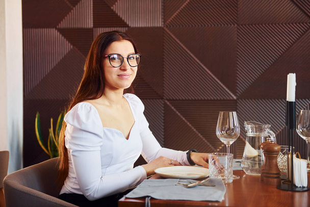 Beautiful woman sits by table. Indoors of new modern luxury restaurant. - Foto, Imagen