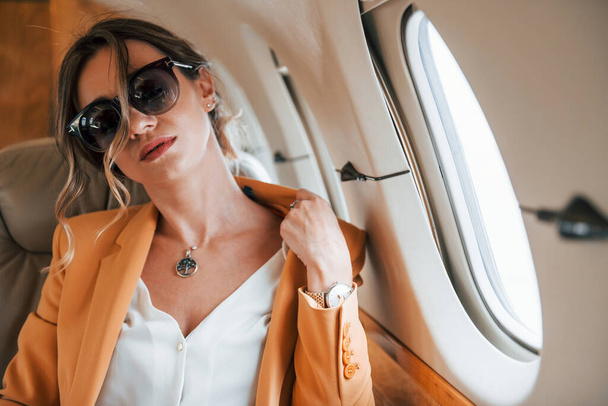 In een zonnebril. Jonge passagier vrouw in gele kleren vliegt in het vliegtuig. - Foto, afbeelding