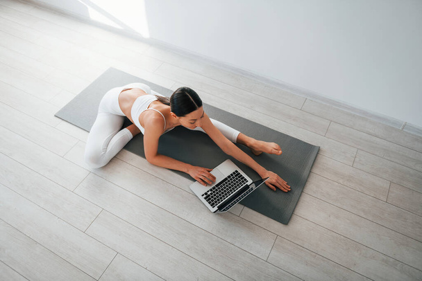 On yoga mat. Young caucasian woman with slim body shape is indoors at daytime. - Valokuva, kuva