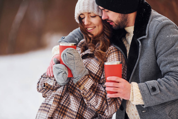 With drink. Cheerful couple have a walk in the winter forest at daytime. - Fotoğraf, Görsel