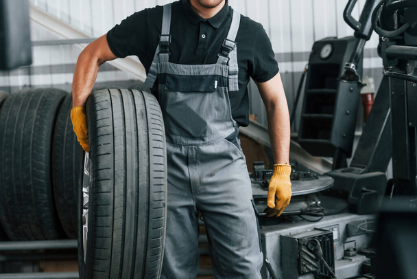 Walking and holding tyre. Man in uniform is working in the auto service. - Foto, imagen