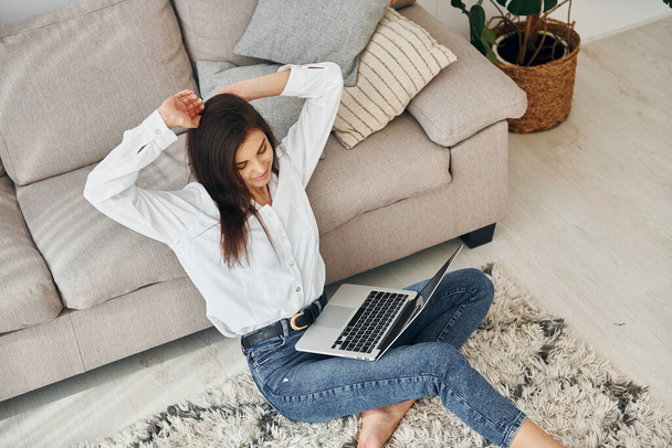 With laptop. Beautiful young woman in jeans and white shirt is at home. - Foto, Imagem