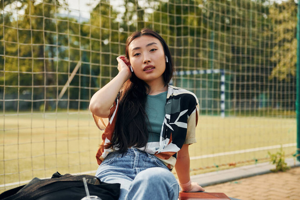 Against net of sport field. Young asian woman is outdoors at daytime. - 写真・画像