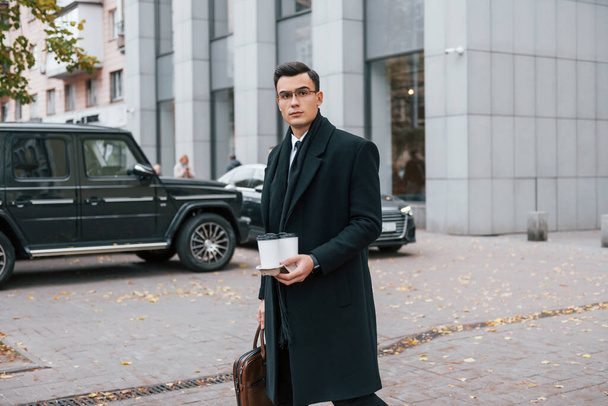 Fresh drink. Businessman in black suit and tie is outdoors in the city. - Fotó, kép