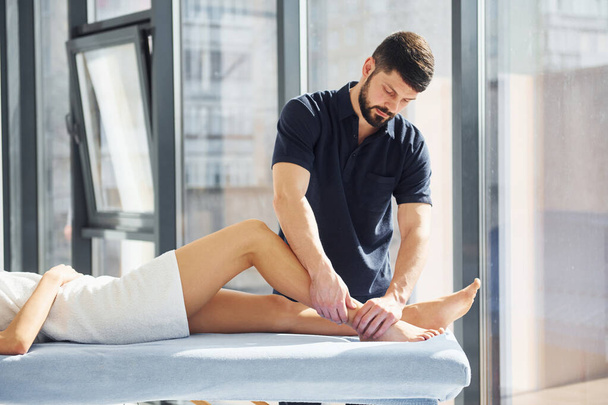 Guy does legs massage. Young woman is lying down when man serves her at spa. - Photo, Image